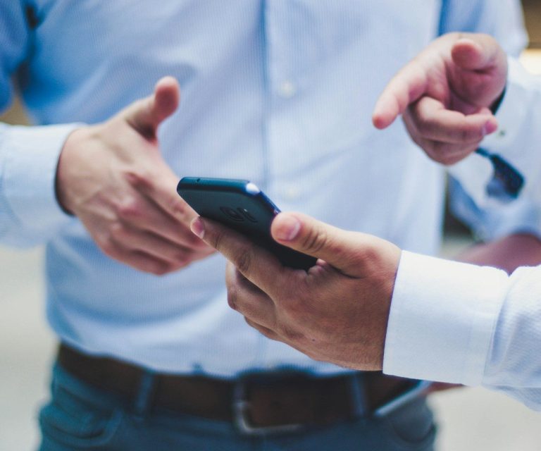 Vorteile einer Messie Entrümpelung in Berlin Zwei Hände halten ein Smartphone, während eine Person darauf zeigt.